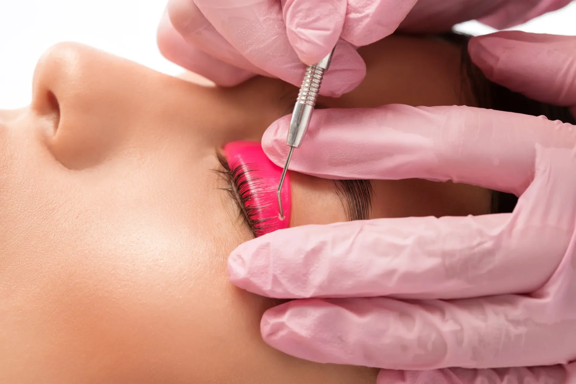 Eyelash extension procedure with pink gloves.