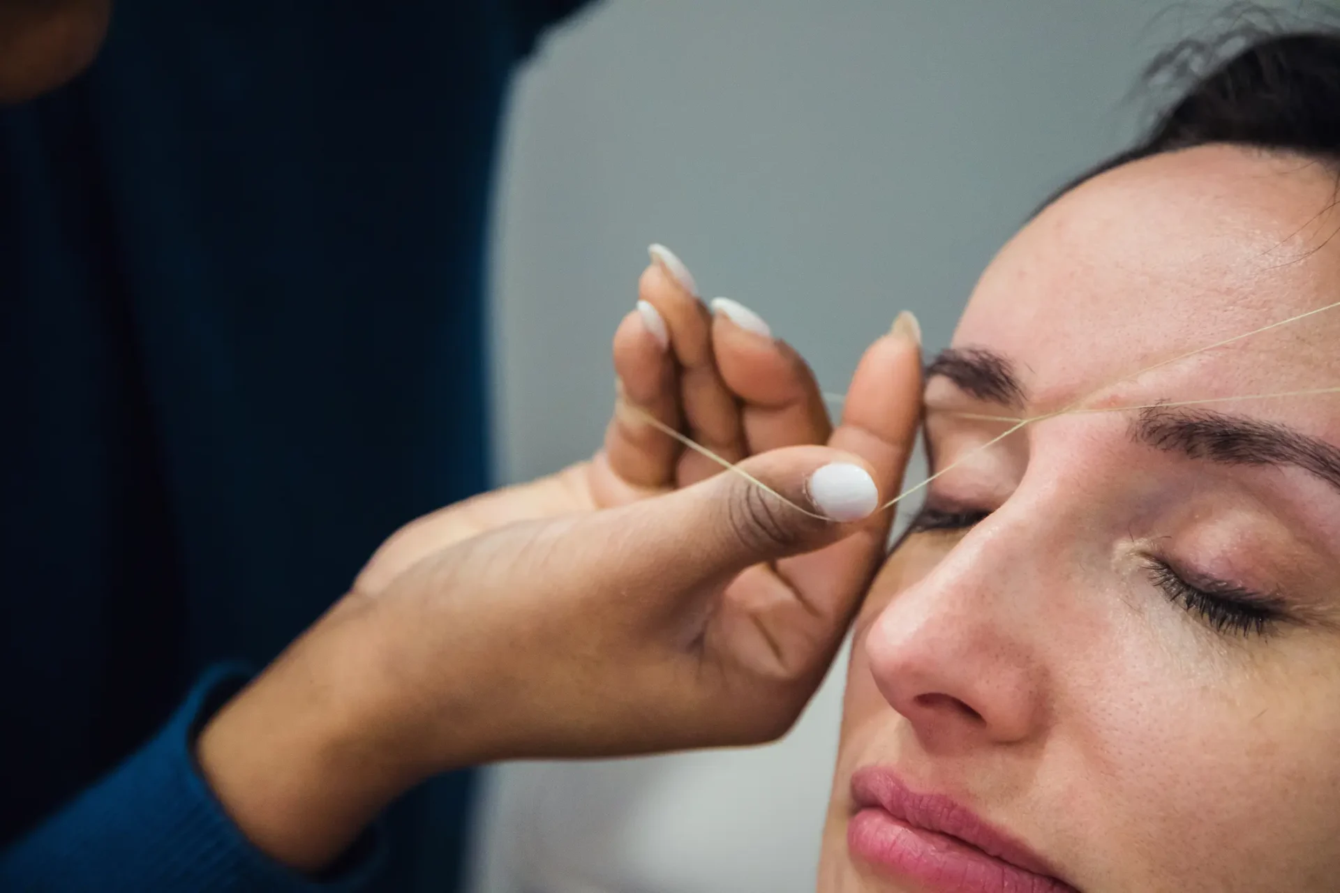 Eyebrow threading procedure on a woman's face.