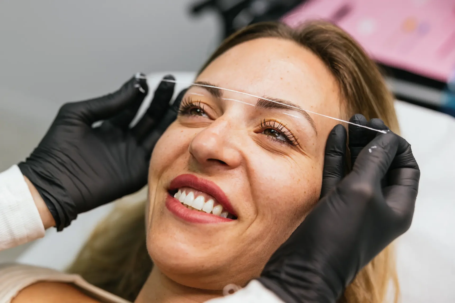 Woman receiving eyebrow threading treatment, smiling.
